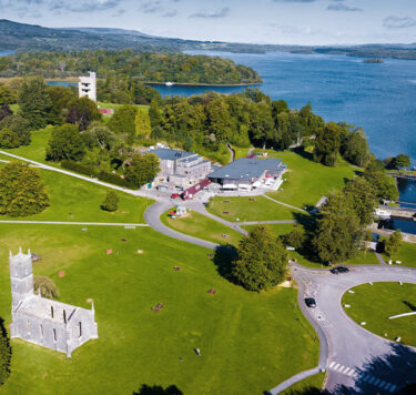 Aerial view of Lough Key Forest Park with green gardens, a historical chapel, and a marina with boats.