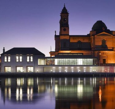 Stunning Luan Gallery with lit historic architecture at dusk, lights reflecting into the river Shannon