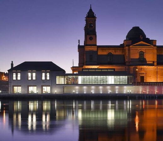 Stunning Luan Gallery with lit historic architecture at dusk, lights reflecting into the river Shannon