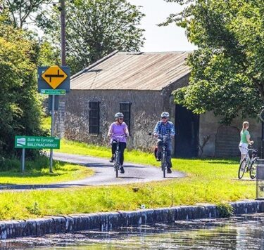 Guests enjoy cycling along a scenic canal path, surrounded by lush greenery and a charming stone building, perfect for a relaxing stay.