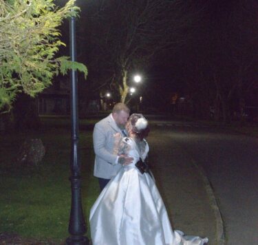 A couple embracing under a lamp post on a serene, tree-lined path at night, with a romantic atmosphere.